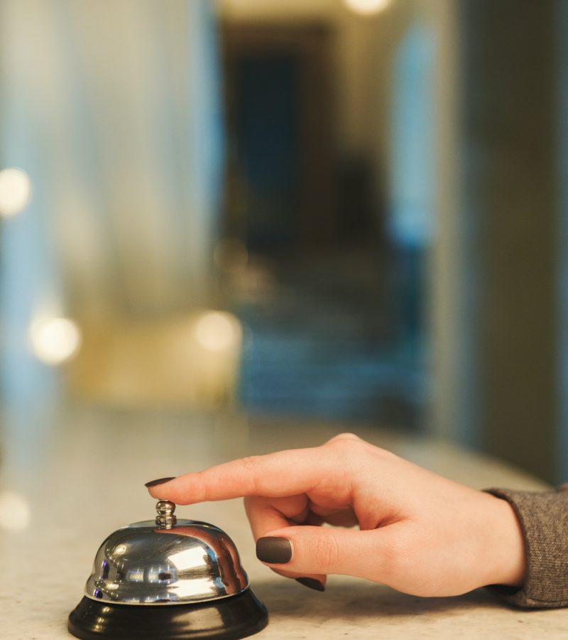 Woman ringing hotel reception service bell closeup